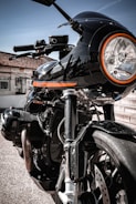 Side view of a motorcycle body with sleek black and orange paint job shining under sunlight.