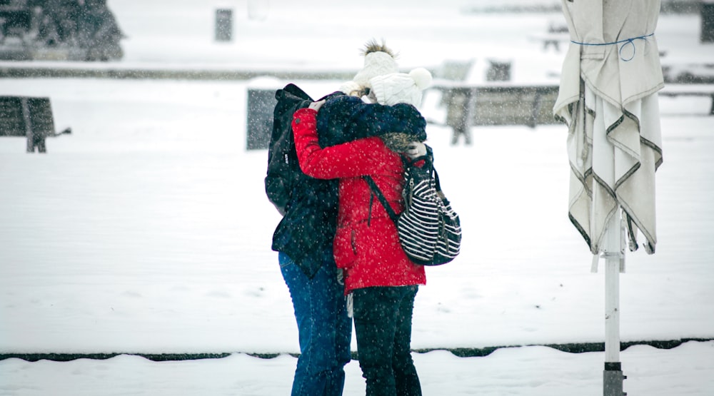 person in red and black jacket and black pants carrying white dog on snow covered ground