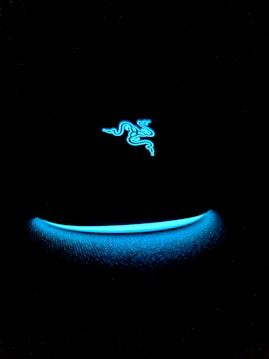 A neon blue logo resembling three intertwining snakes is set against a black background. Below, a softly glowing blue arc adds to the Futuristic vibe.