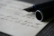 A hand comfortably gripping a smooth fountain pen, writing on crisp white paper.