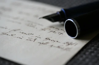 Close-up of a hand holding a classic fountain pen poised over a blank sheet of paper.