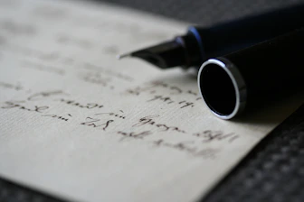 Close-up of hands signing a legal contract with a fountain pen on a gray and white background.