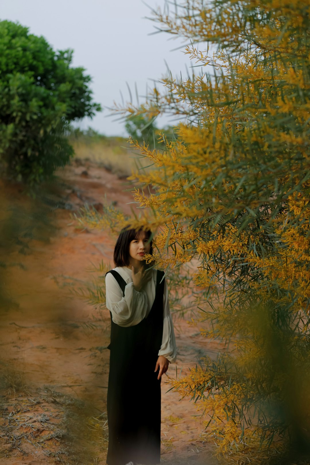 woman in white long sleeve shirt and black skirt standing near green tree during daytime