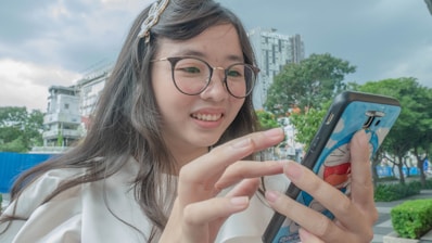 A happy young woman using her smartphone outdoors with a city skyline in the background.