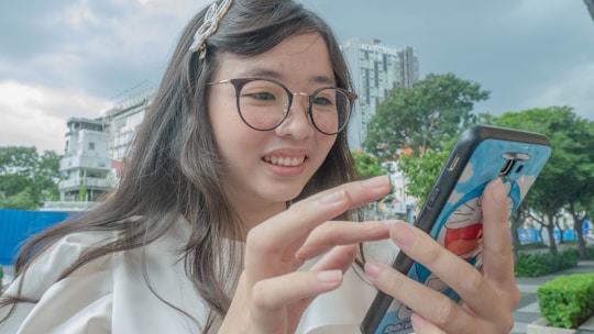 A happy young woman using her smartphone outdoors with a bright cityscape in the background.