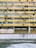 A multi-story building facade with a worn yellow exterior. Rows of windows, many with air conditioning units mounted alongside them. A sign in both English and Chinese directs towards a lift lobby. The walls appear aged with visible rust and stains.