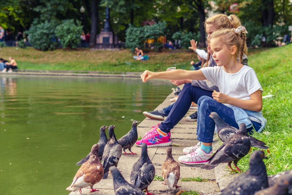 girl in white t-shirt and blue denim jeans sitting on brown wooden bench