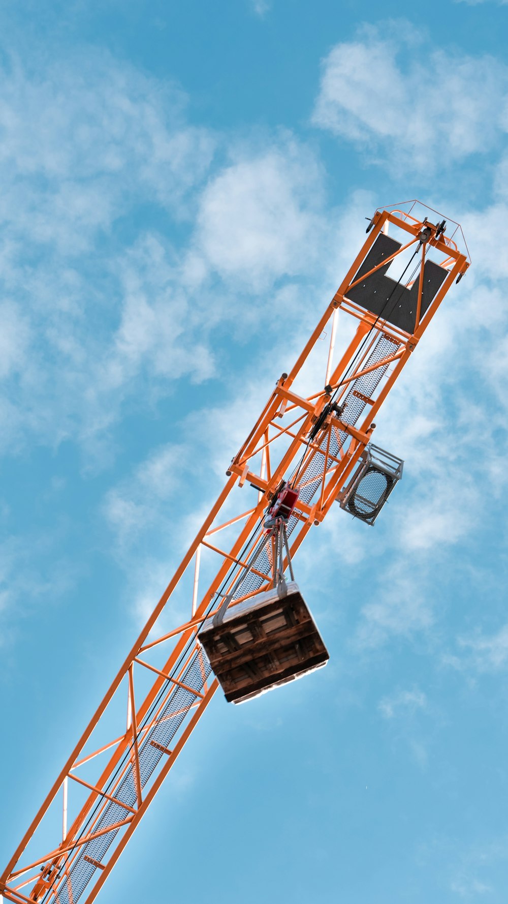 orange and black tower crane under blue sky