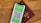 A smartphone displaying a digital COVID-19 passport with a QR code is placed on top of a maroon-colored physical passport. The digital document is green with text and a black and white QR code, while the physical passport has gold embossed lettering.