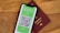 A smartphone displaying a digital COVID-19 passport with a QR code is placed on top of a maroon-colored physical passport. The digital document is green with text and a black and white QR code, while the physical passport has gold embossed lettering.
