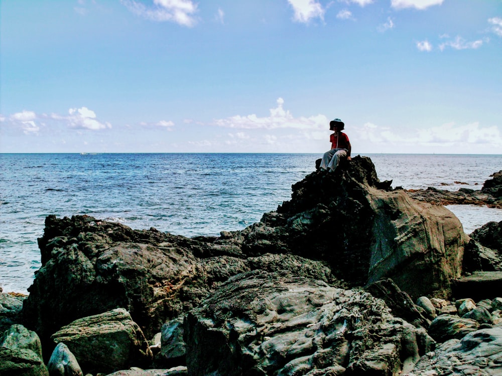 man in black jacket standing on rock formation near sea during daytime