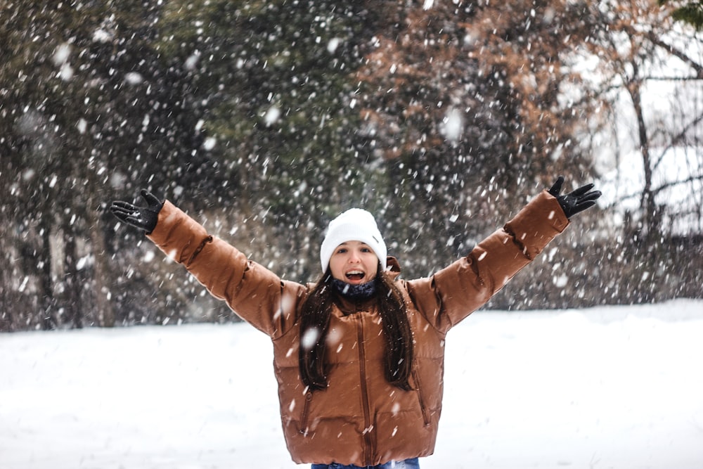 woman in brown jacket and white knit cap standing on snow covered ground during daytime