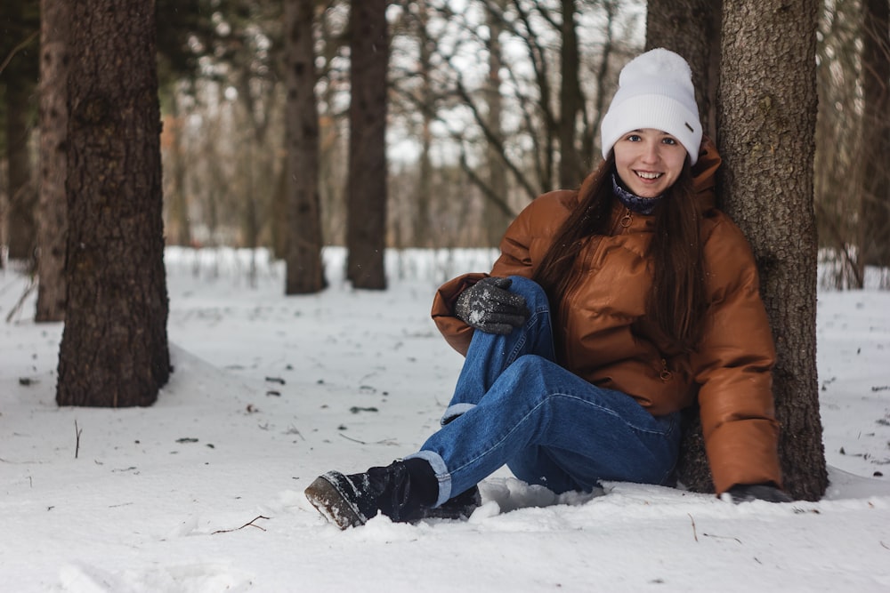 woman in brown jacket and blue denim jeans sitting on snow covered ground during daytime