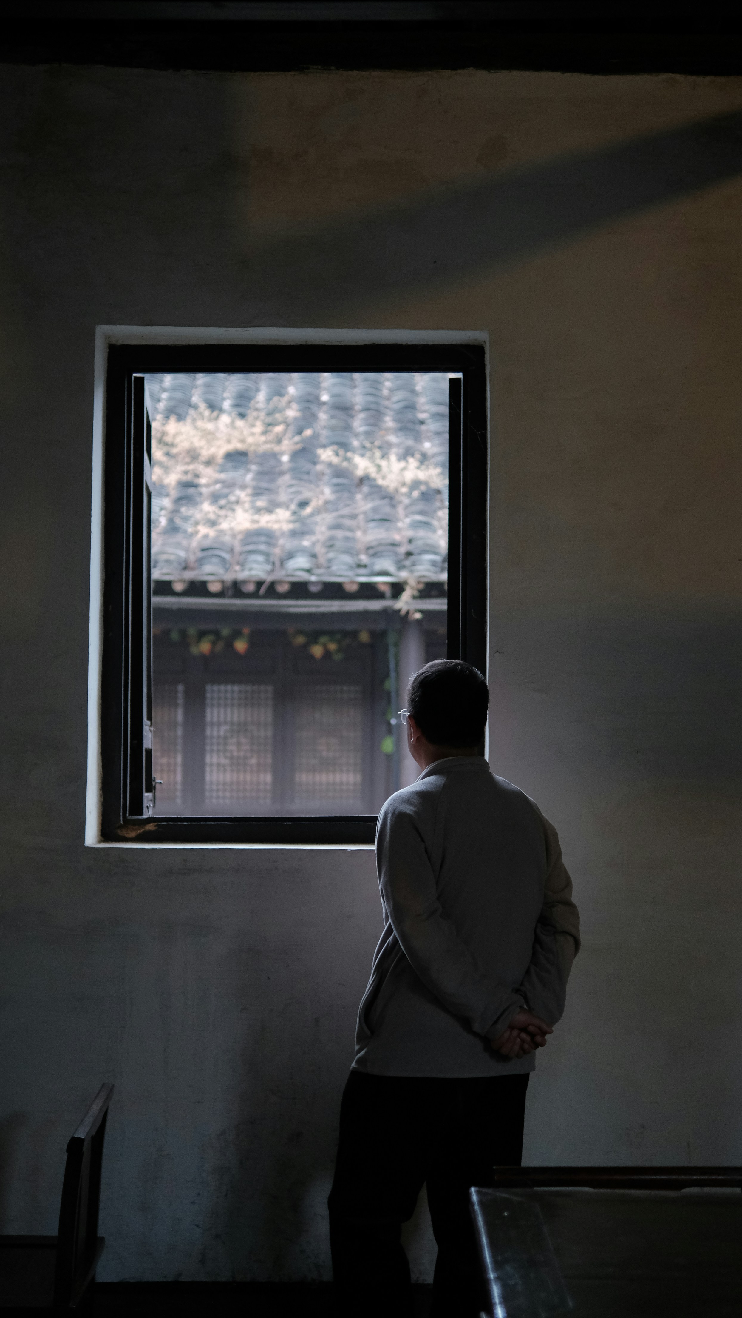Hombre con abrigo gris de pie cerca de la ventana