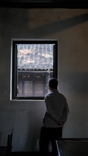 A quiet moment of reflection by a window in a UK accommodation, capturing the spirit of perseverance.