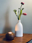 Close-up of a textured glass candle lit softly beside a vase of fresh spring flowers