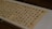 A piece of traditional East Asian calligraphy in black ink on a light beige paper, featuring neatly arranged characters in vertical columns. The writing is enclosed in a glass frame, and there are red seals stamped near the edges.
