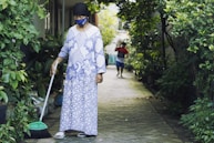 woman in white and blue floral long sleeve dress holding green broom