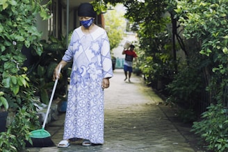 woman in white and blue floral long sleeve dress holding green broom