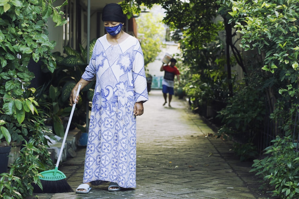 woman in white and blue floral long sleeve dress holding green broom