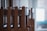 Wooden chairs are stacked in an orderly manner inside a room. Natural light filters through a window in the background, creating a calm and serene atmosphere.