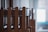 Wooden chairs are stacked in an orderly manner inside a room. Natural light filters through a window in the background, creating a calm and serene atmosphere.