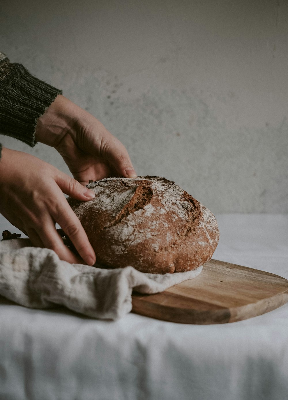 Persona che tiene il pane integrale sul tagliere di legno marrone