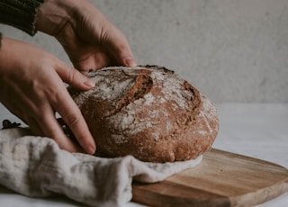 person holding brown bread on brown wooden chopping board