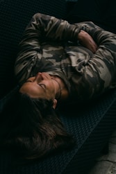 woman in gray and black camouflage jacket lying on black couch