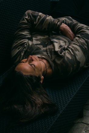 woman in gray and black camouflage jacket lying on black couch