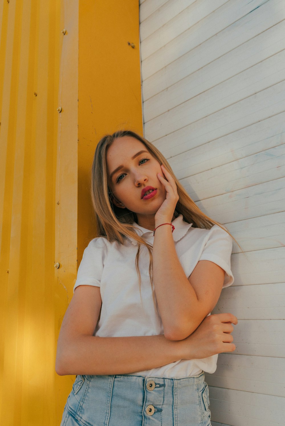 woman in white shirt leaning on yellow wall