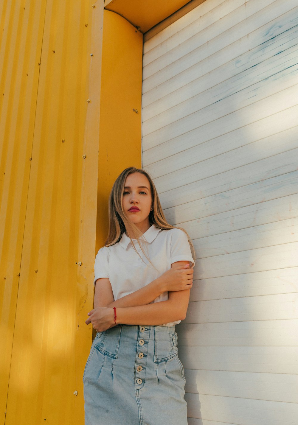 woman in white shirt and blue denim shorts standing beside yellow wall