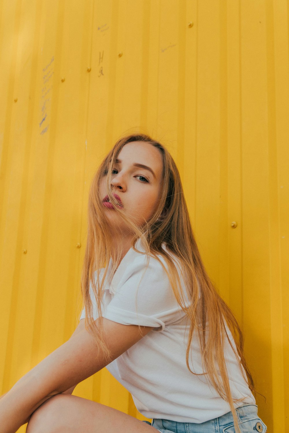 woman in white shirt leaning on yellow wall
