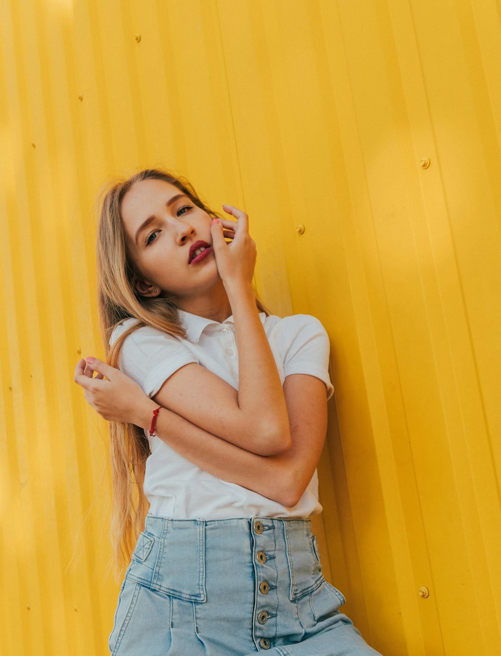 woman in white tank top and blue denim shorts leaning on yellow wall