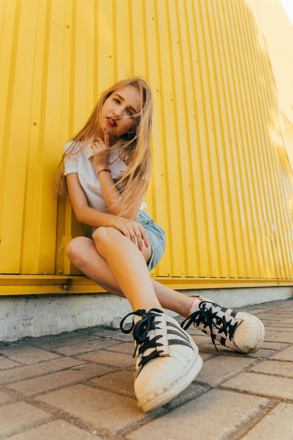 woman in white t-shirt and blue denim shorts sitting on concrete floor