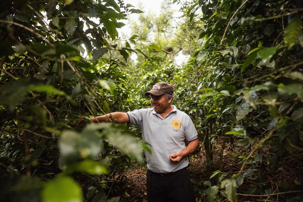 man in white crew neck t-shirt standing in the middle of the forest during daytime