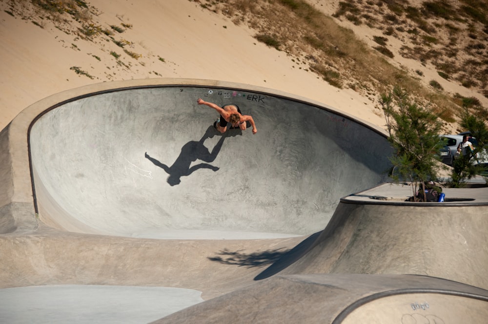 homme en veste noire et pantalon noir faisant des cascades sur la rampe de skateboard pendant la journée