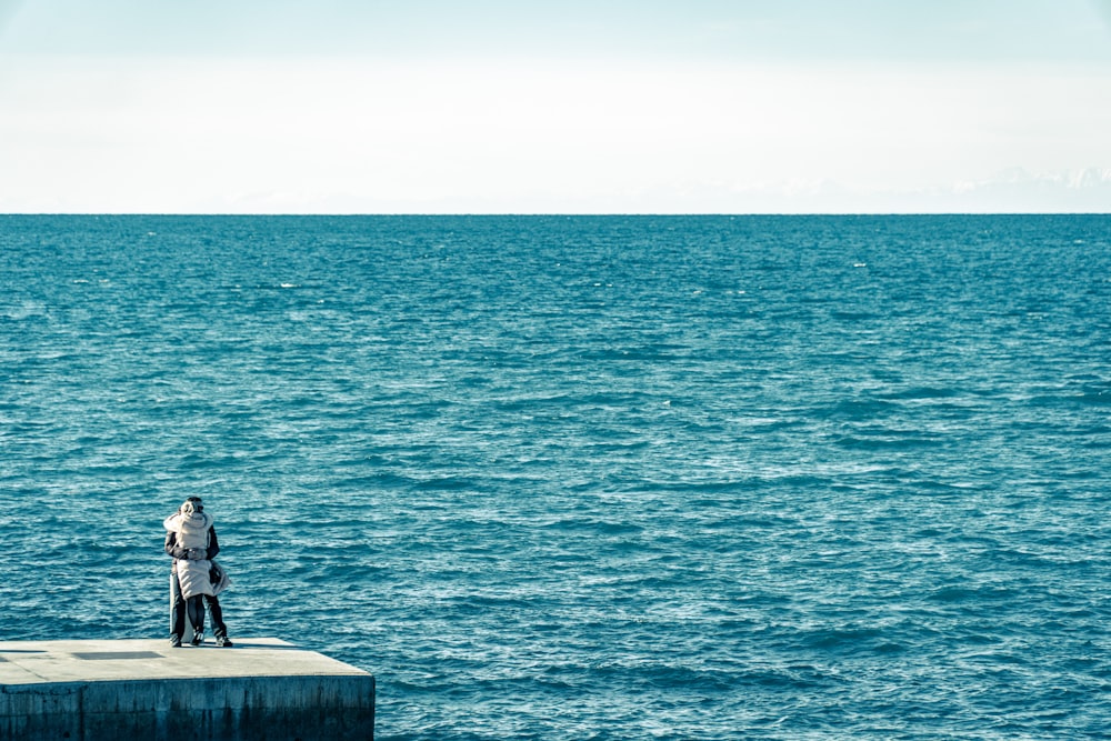 Mann in schwarzer Jacke sitzt tagsüber auf einer Betonbank in der Nähe des Meeres