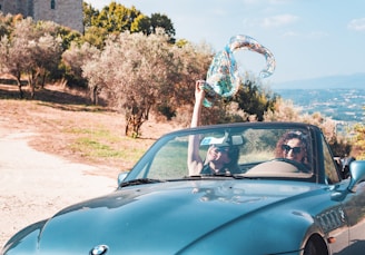 A couple enjoying a scenic drive in a convertible with Altinho hills in the background.