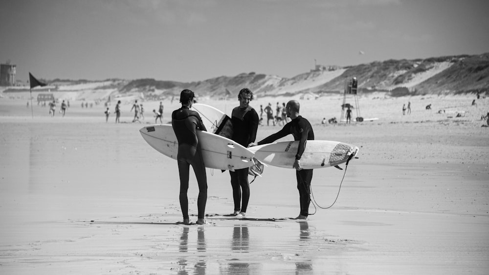 grayscale photo of 2 men and woman holding surfboard walking on beach
