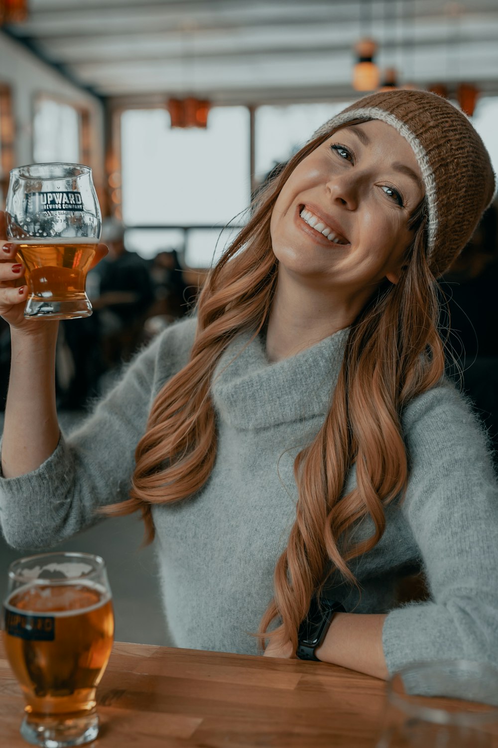 smiling woman in gray sweater holding clear drinking glass with brown liquid