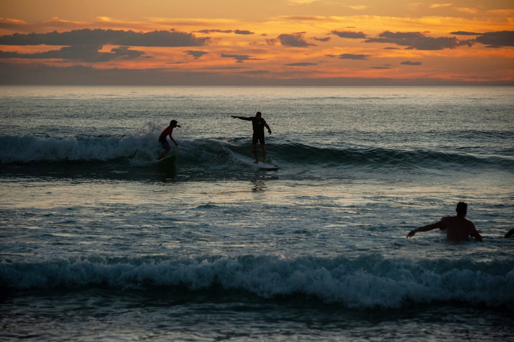 2 person surfing on sea waves during sunset