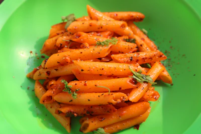 Colorful plate of penne pasta with grilled vegetables and a drizzle of olive oil.