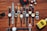 A collection of various wristwatches is arranged neatly on a wooden surface, displaying a range of designs and colors. Dice, sunglasses, a red toy car, and a yellow bottle labeled 'English Blazer Victory' are also present, adding to the display's eclectic mix.