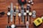 A collection of various wristwatches is arranged neatly on a wooden surface, displaying a range of designs and colors. Dice, sunglasses, a red toy car, and a yellow bottle labeled 'English Blazer Victory' are also present, adding to the display's eclectic mix.