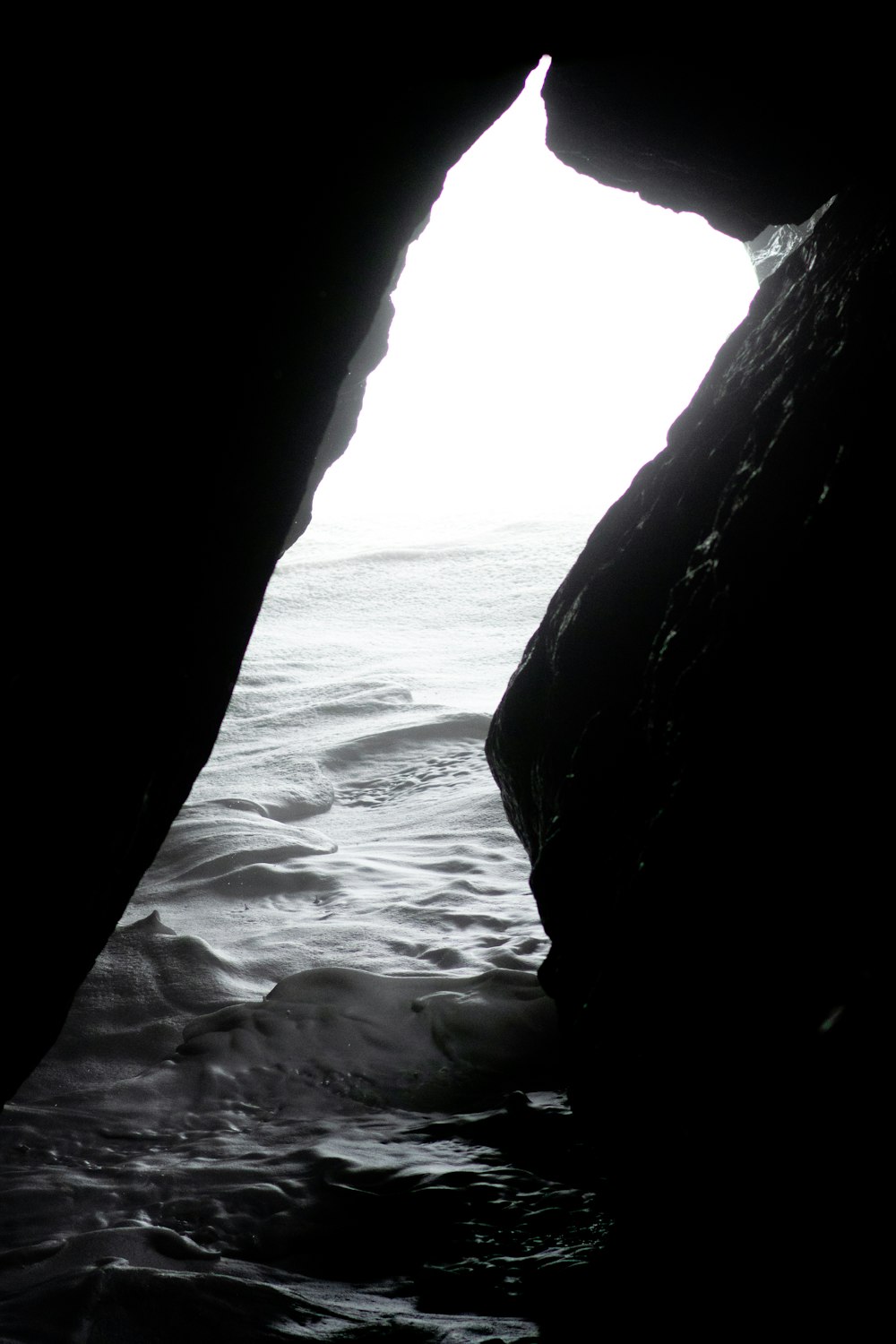grayscale photo of cave near body of water