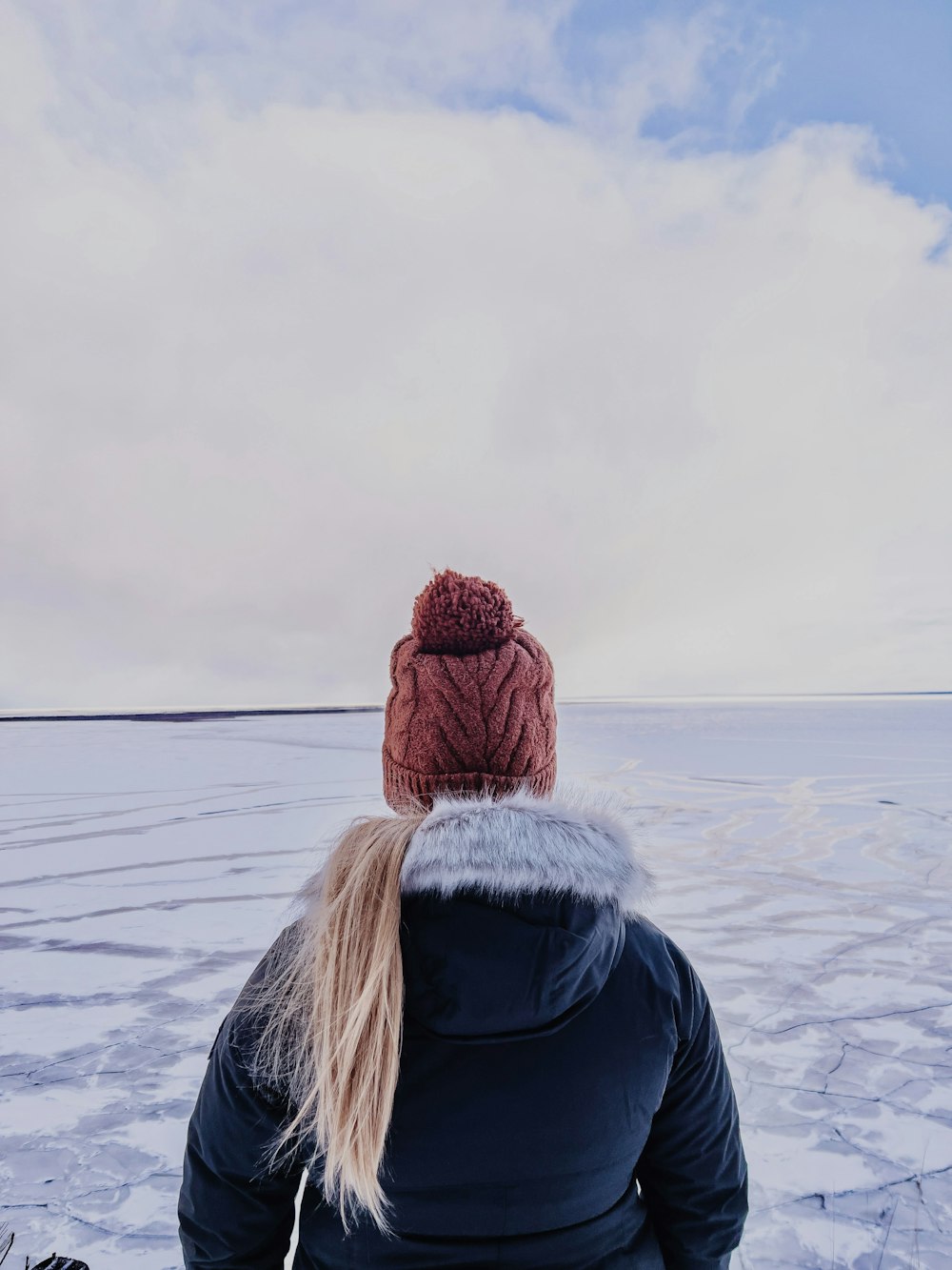 woman in black jacket and red knit cap standing on snow covered ground during daytime