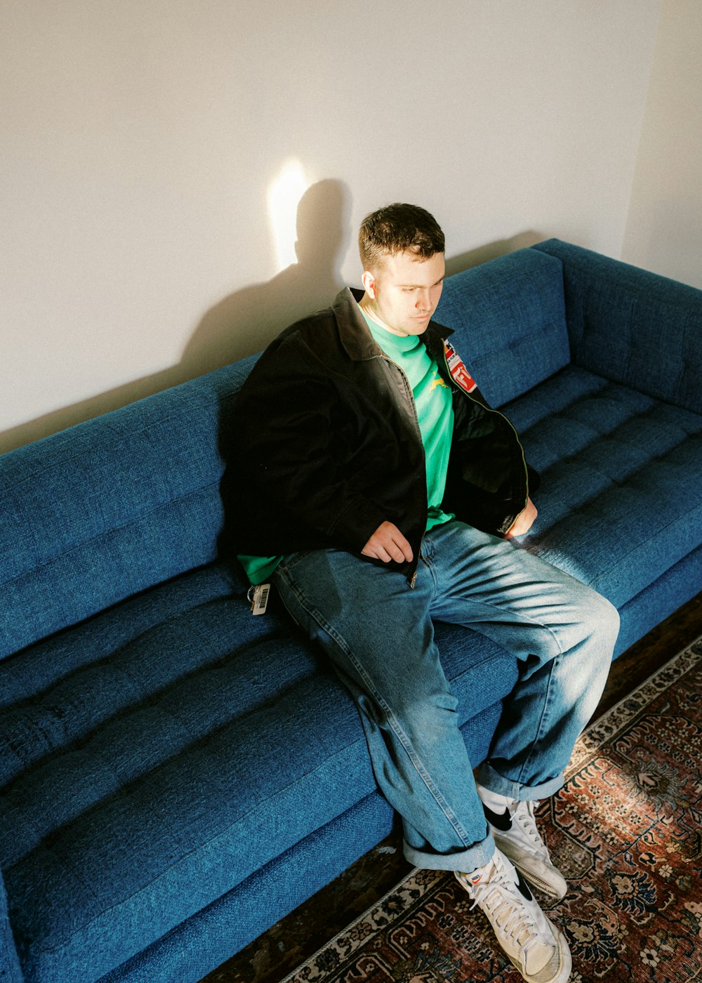 man in black jacket and blue denim jeans sitting on blue couch