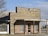A rustic barbecue restaurant with a wooden facade displaying the sign 'Pody's BBQ'. The building has a covered entrance with metal bars on the windows and a combination of brick and wood materials. It's situated in a seemingly rural or small-town setting with clear skies.