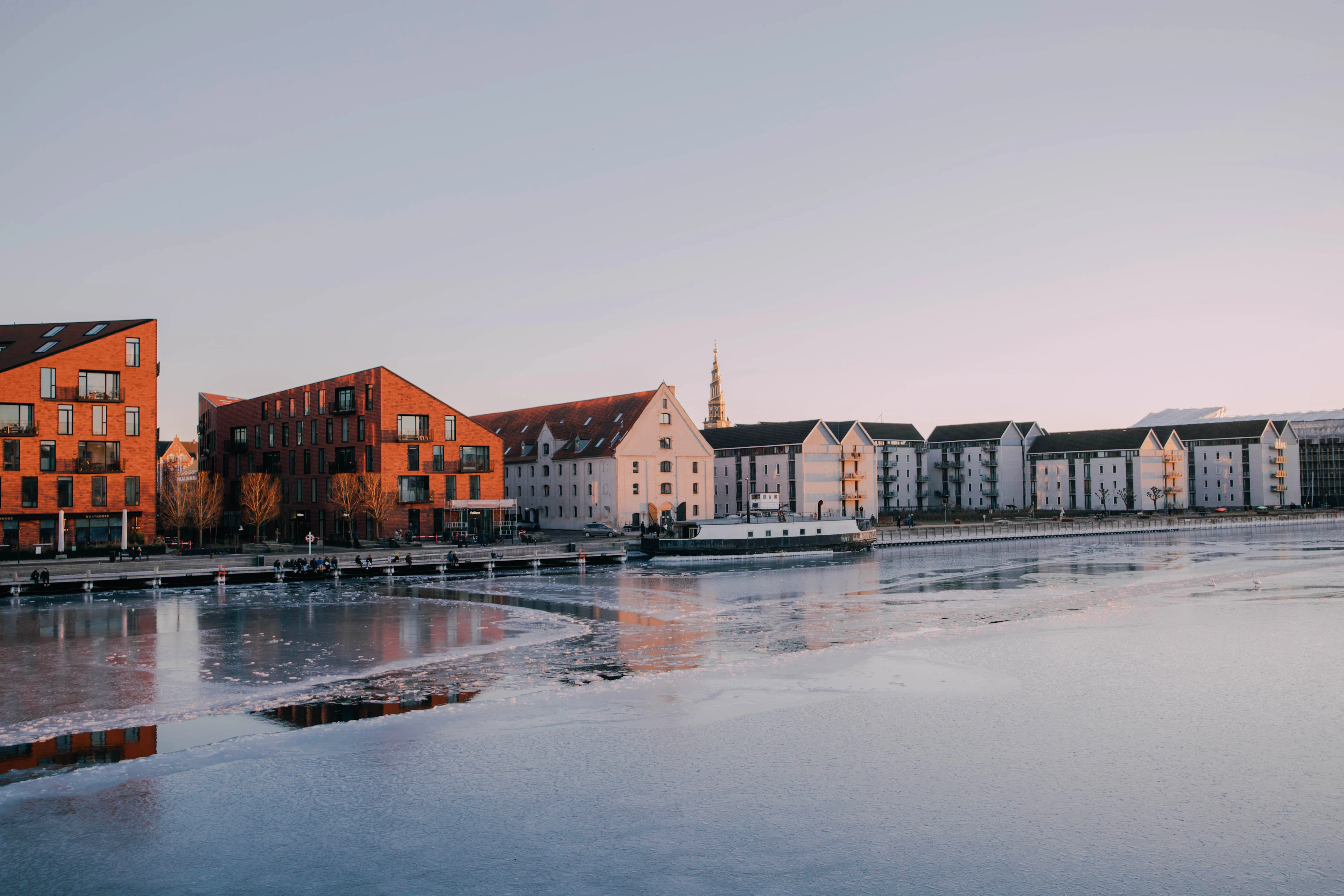 Flerbostadshus i tegel och trä vid en å i solnedgång